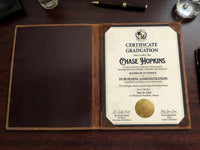 Graduation certificate in a leather holder on a wooden surface