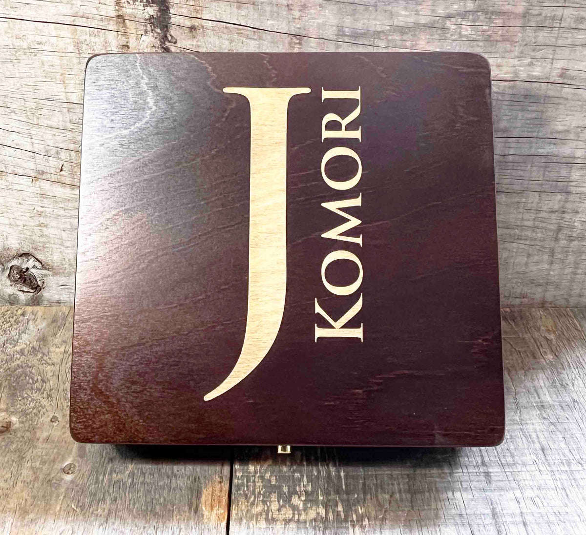 Wooden box with 'J Komori' branding on a wooden surface