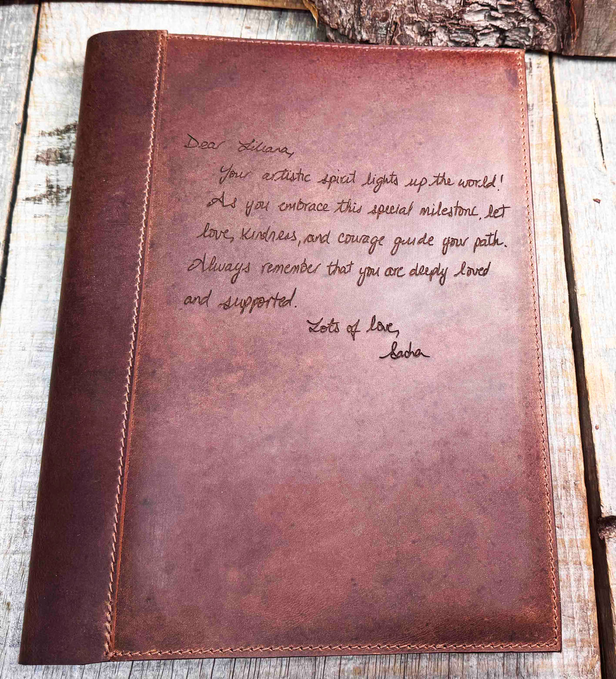 A brown, custom-engraved leather notebook cover featuring a geometric unicorn head design. The notebook is resting on an antique-style, ornate wooden desk alongside a glass inkwell and a feathered quill pen, creating a sophisticated and vintage aesthetic.