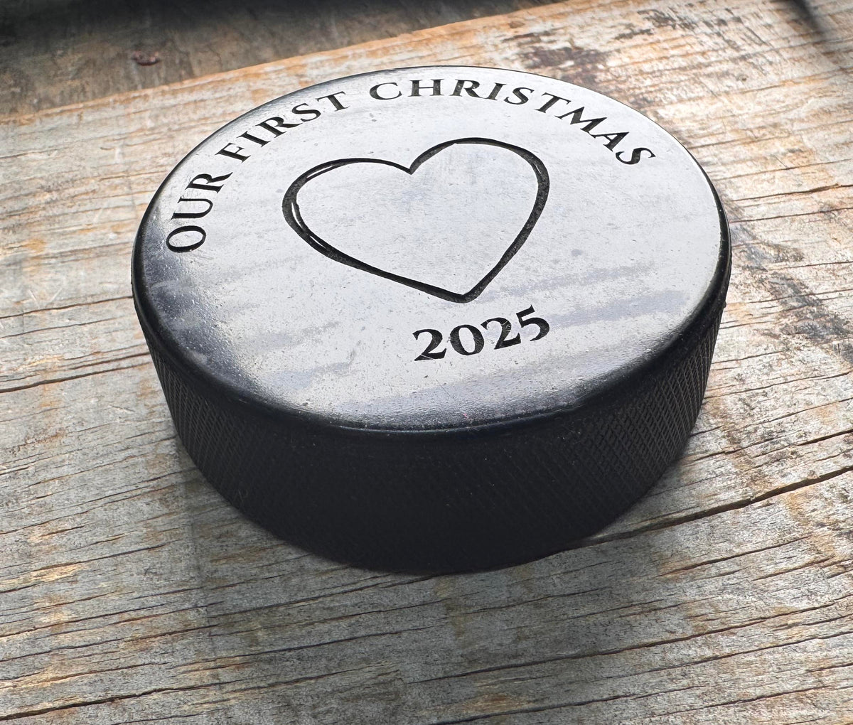 Hockey puck with 'Our First Christmas 2025' engraving on a wooden surface