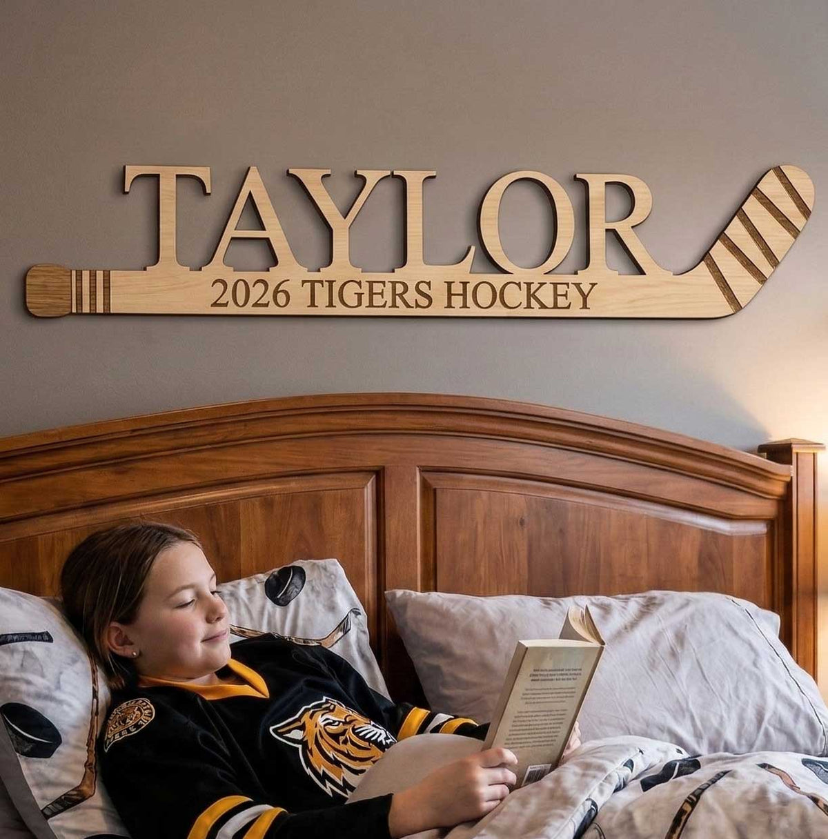 Person in a hockey jersey reading a book in bed with a personalized wooden sign above the bed.