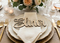 Table setting with 'Elinor' name card, plates, and cutlery on a wooden table.