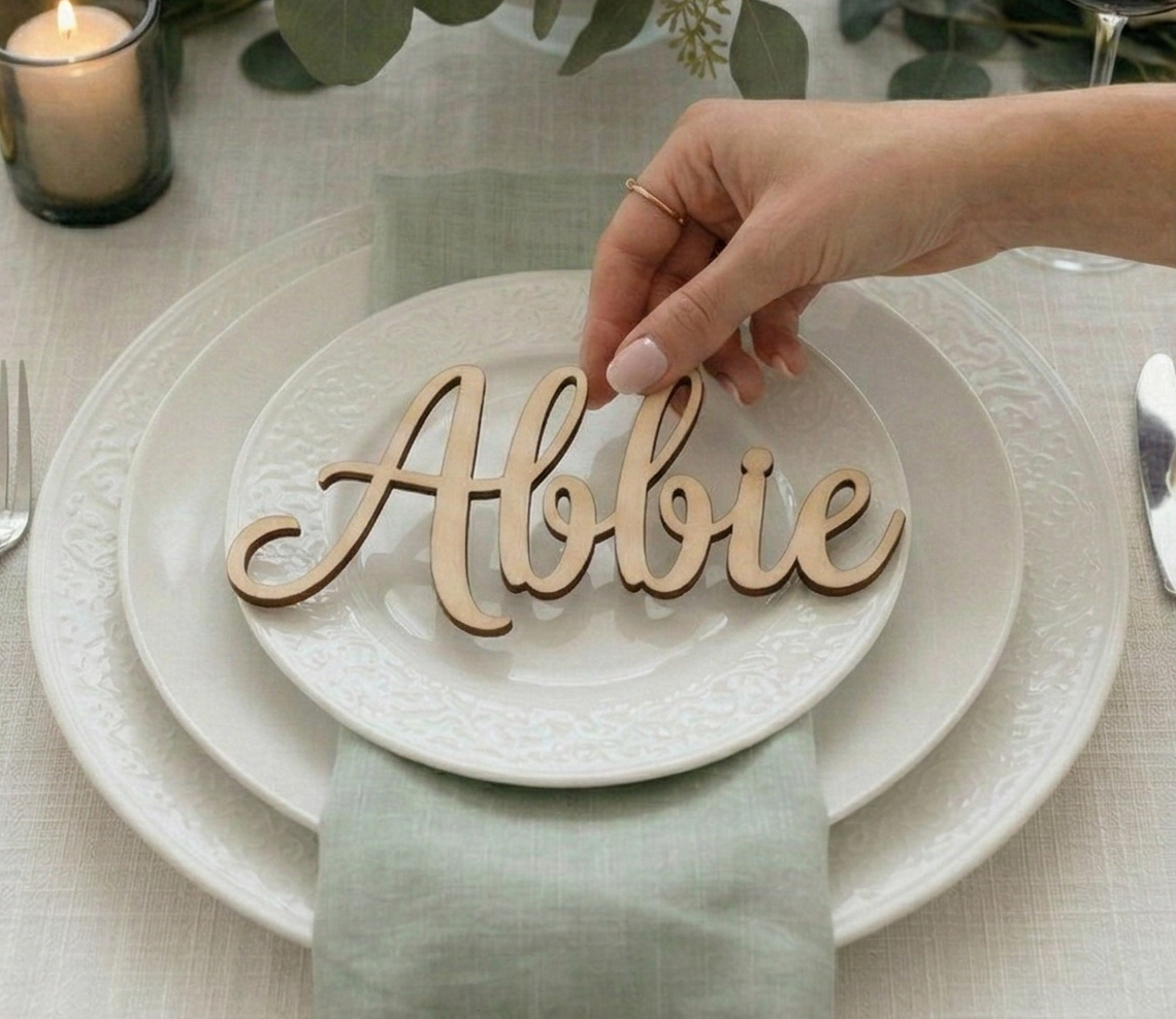 Hand placing a wooden name card with 'Abbie' on a set table.