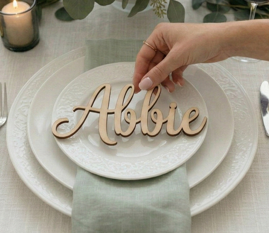 Hand placing a wooden name card with 'Abbie' on a set table.