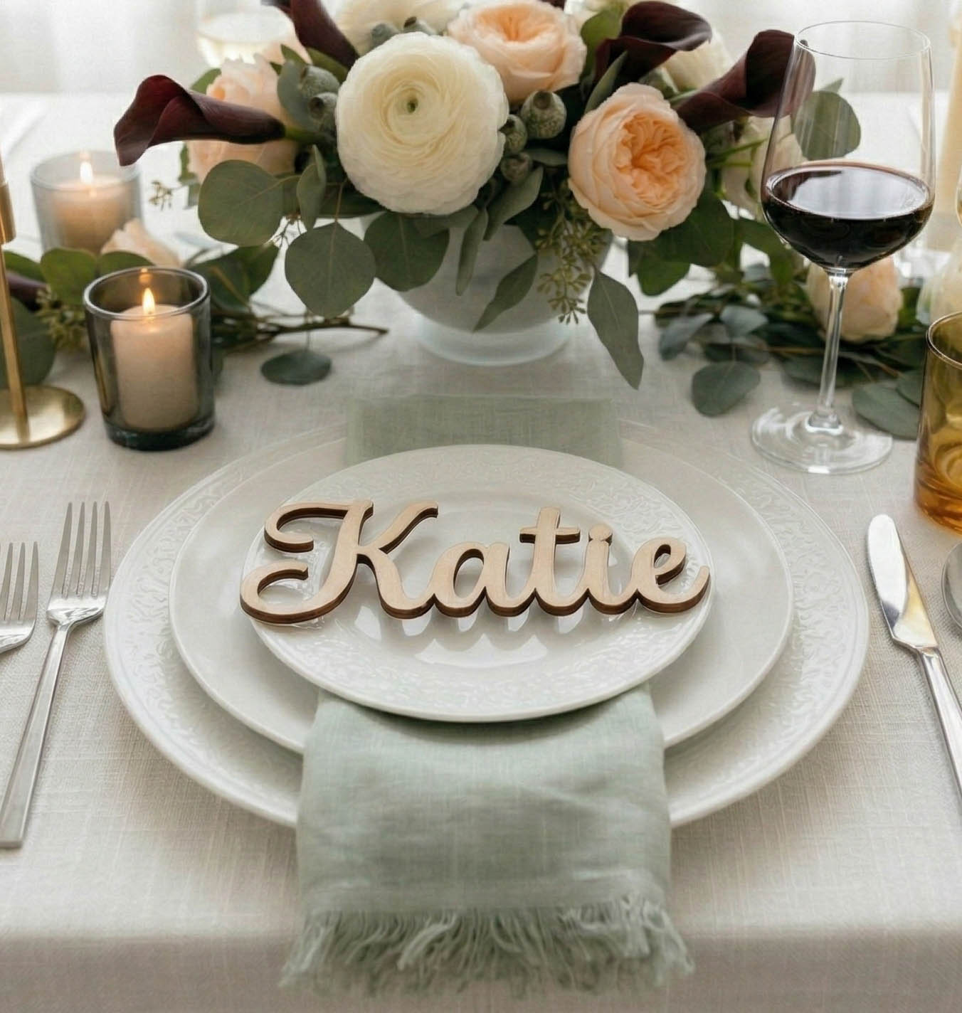 Table setting with floral arrangement, candles, and a name card on a white tablecloth.