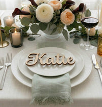 Table setting with floral arrangement, candles, and a name card on a white tablecloth.