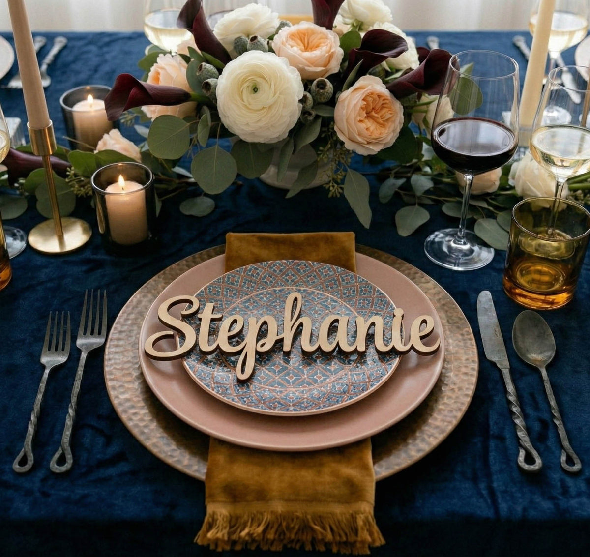 Elegant table setting with floral arrangement, candles, and 'Stephanie' name card on a blue tablecloth.
