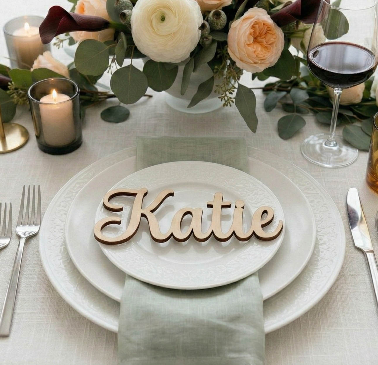 Table setting with a name card labeled 'Katie' on a white plate, surrounded by flowers and candles.