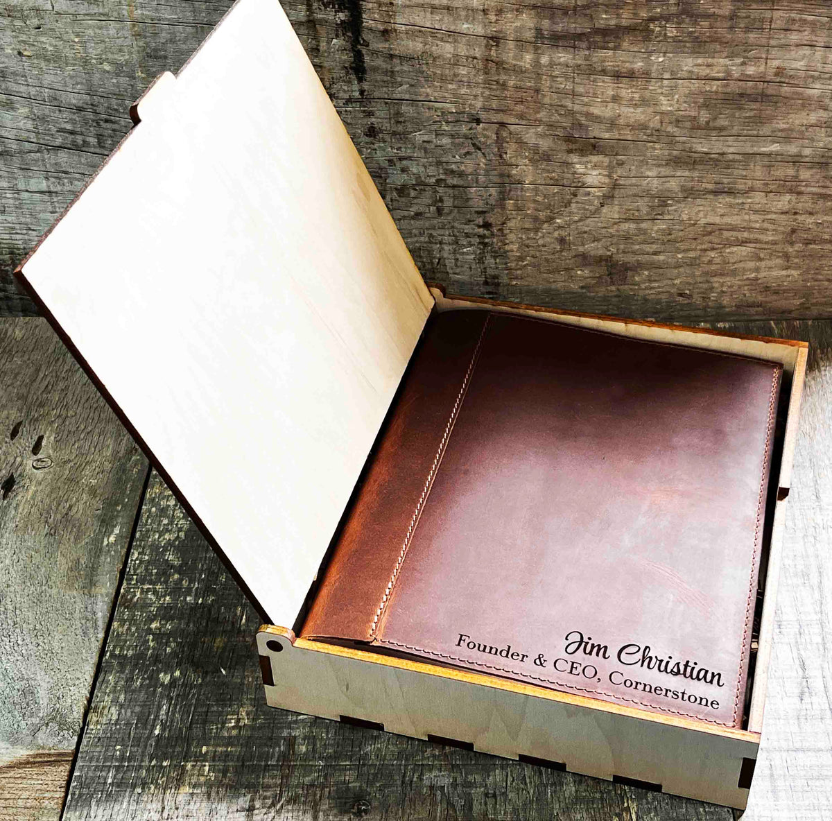 A brown, custom-engraved leather notebook cover featuring a geometric unicorn head design. The notebook is resting on an antique-style, ornate wooden desk alongside a glass inkwell and a feathered quill pen, creating a sophisticated and vintage aesthetic.