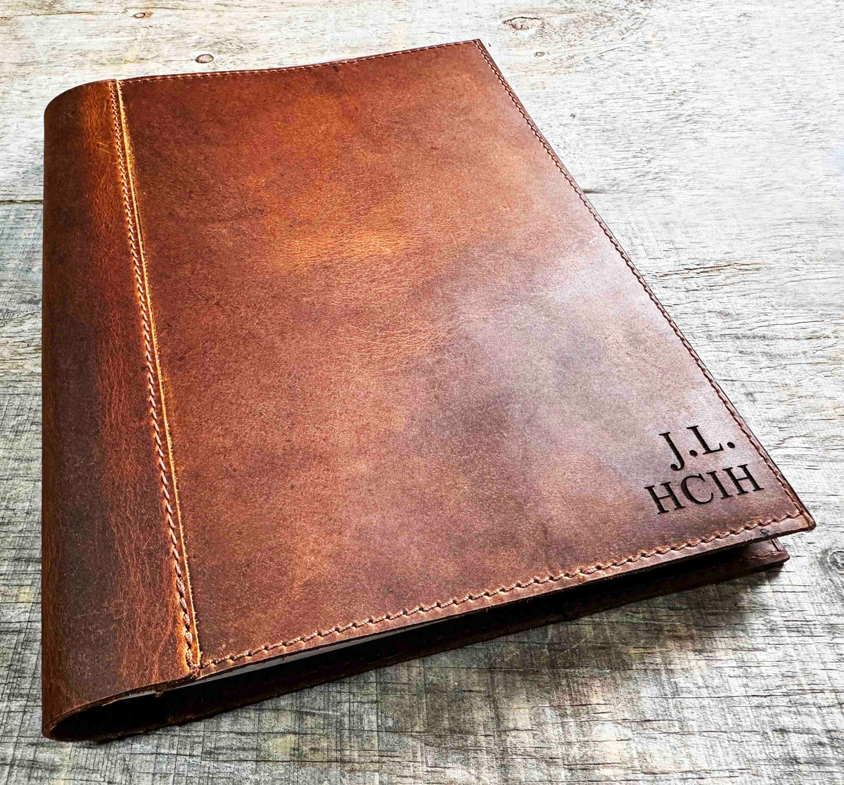 A brown, custom-engraved leather notebook cover featuring a geometric unicorn head design. The notebook is resting on an antique-style, ornate wooden desk alongside a glass inkwell and a feathered quill pen, creating a sophisticated and vintage aesthetic.