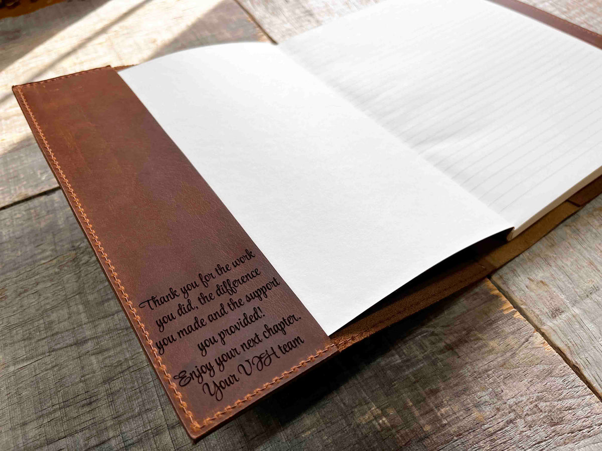 A brown, custom-engraved leather notebook cover featuring a geometric unicorn head design. The notebook is resting on an antique-style, ornate wooden desk alongside a glass inkwell and a feathered quill pen, creating a sophisticated and vintage aesthetic.