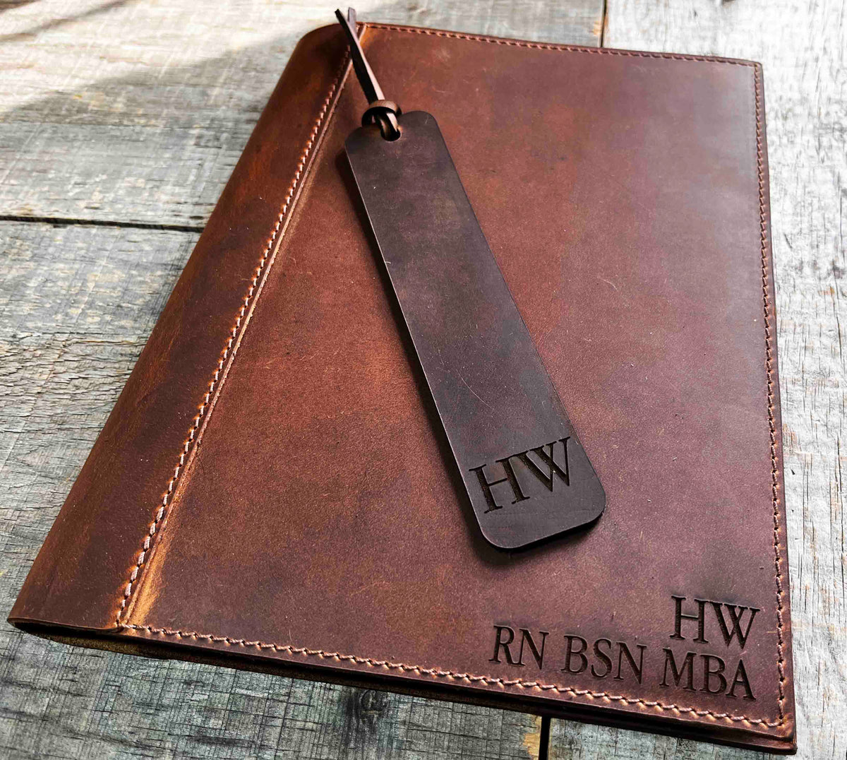 A brown, custom-engraved leather notebook cover featuring a geometric unicorn head design. The notebook is resting on an antique-style, ornate wooden desk alongside a glass inkwell and a feathered quill pen, creating a sophisticated and vintage aesthetic.