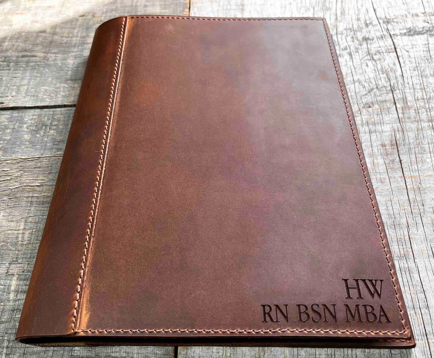 A brown, custom-engraved leather notebook cover featuring a geometric unicorn head design. The notebook is resting on an antique-style, ornate wooden desk alongside a glass inkwell and a feathered quill pen, creating a sophisticated and vintage aesthetic.