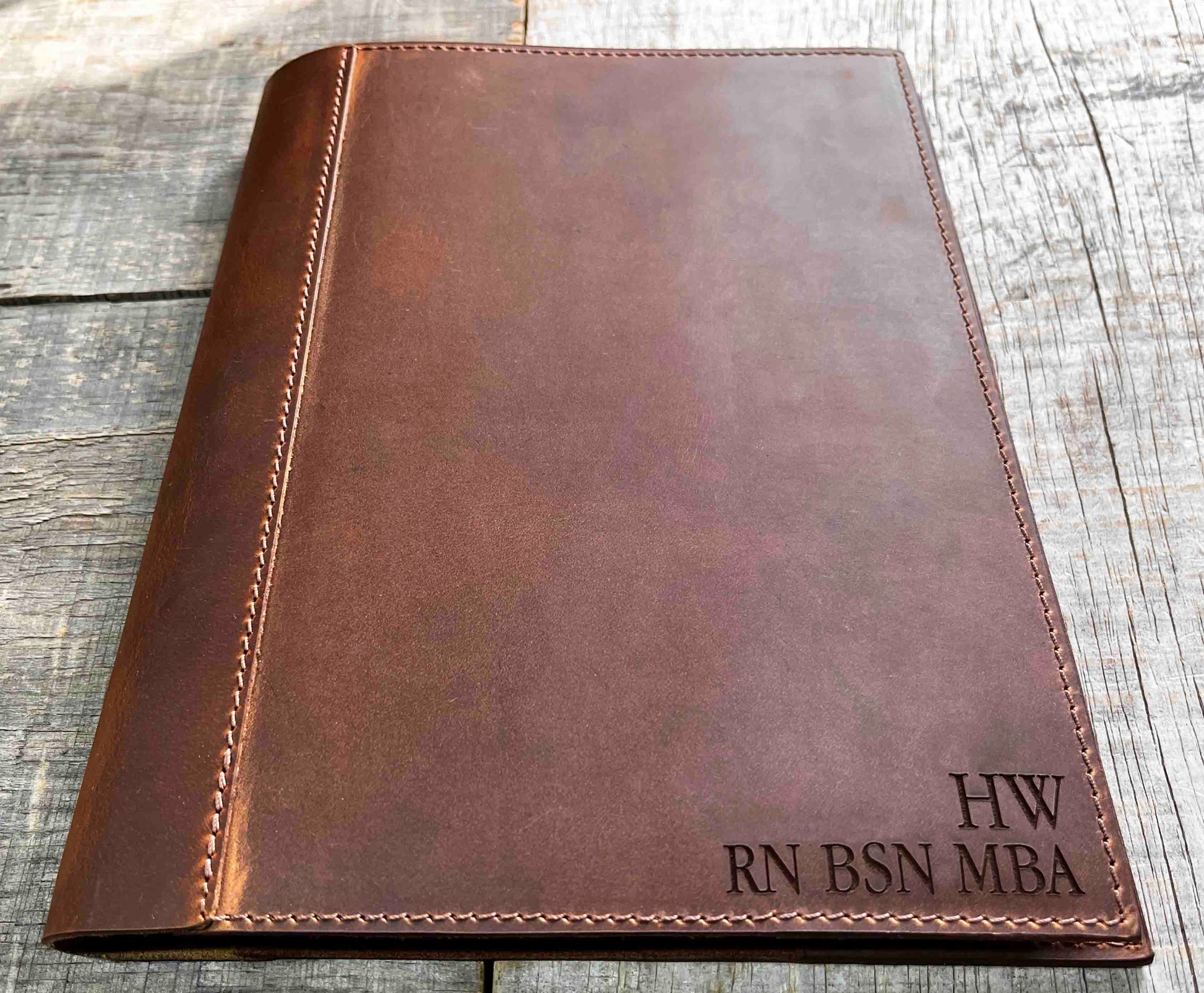 A brown, custom-engraved leather notebook cover featuring a geometric unicorn head design. The notebook is resting on an antique-style, ornate wooden desk alongside a glass inkwell and a feathered quill pen, creating a sophisticated and vintage aesthetic.