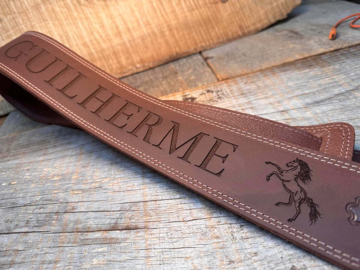 Brown leather strap with 'GUILHERME' engraving on a wooden surface