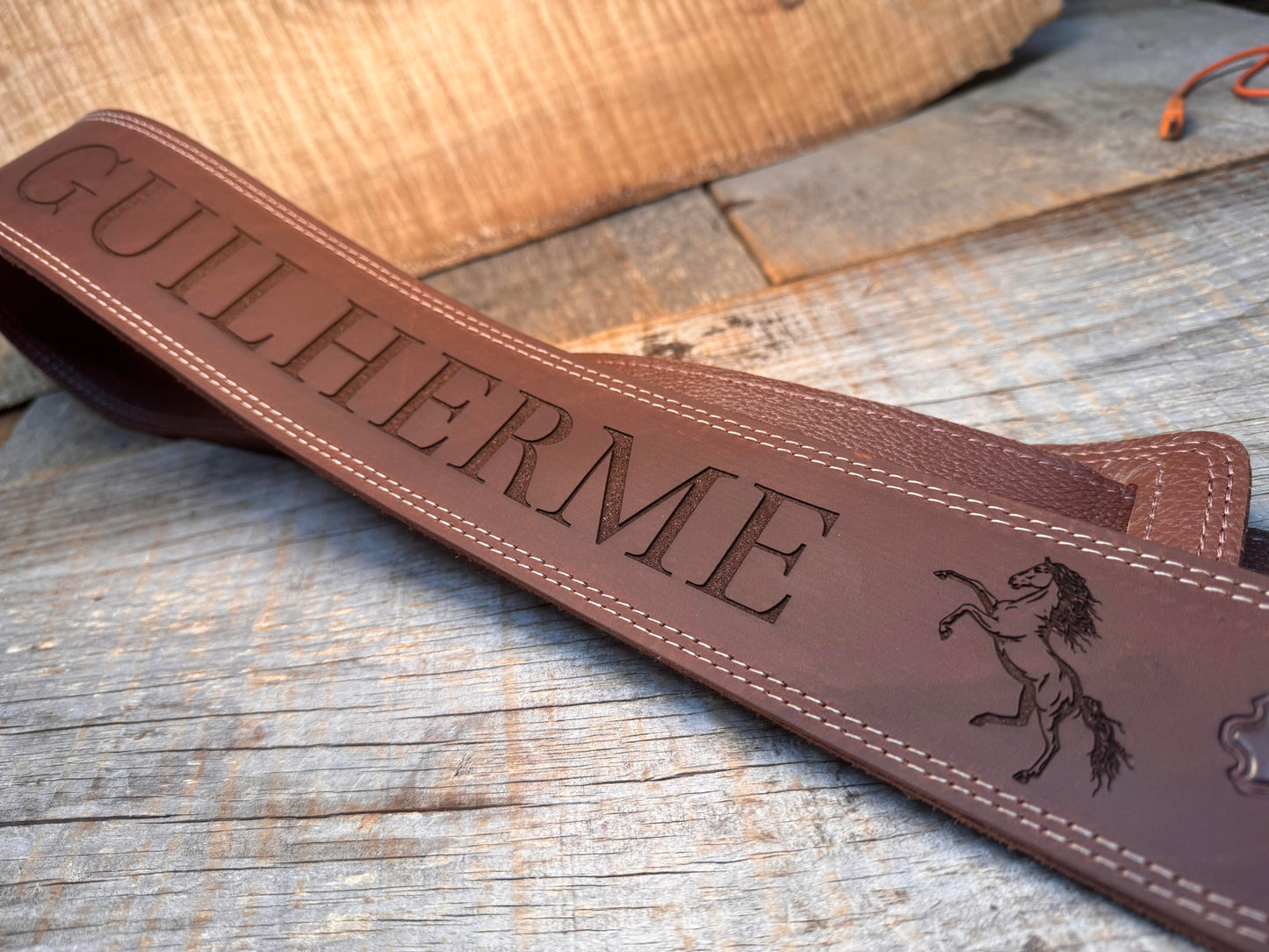 Brown leather strap with 'GUILHERME' engraving on a wooden surface