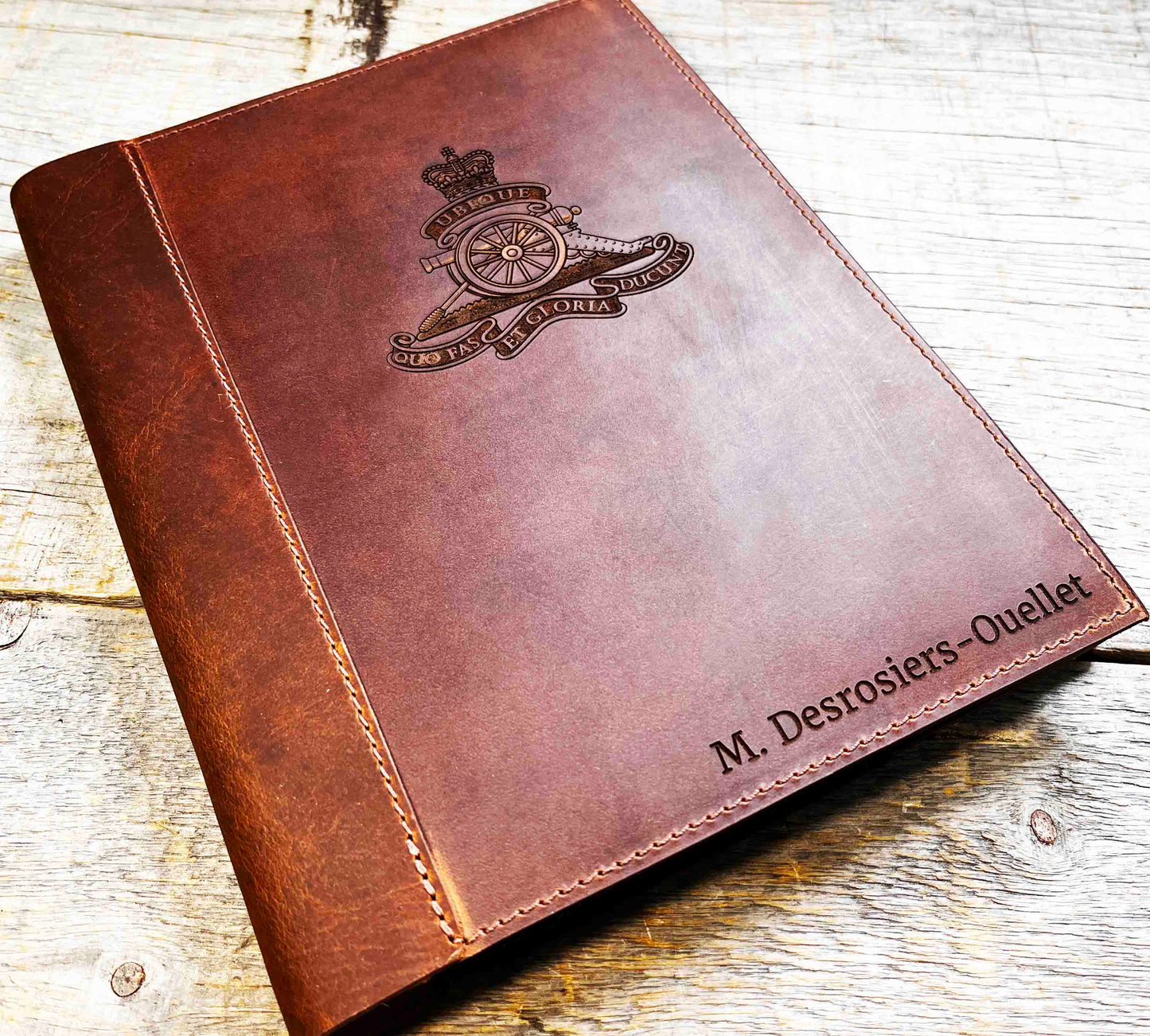 A brown, custom-engraved leather notebook cover featuring a geometric unicorn head design. The notebook is resting on an antique-style, ornate wooden desk alongside a glass inkwell and a feathered quill pen, creating a sophisticated and vintage aesthetic.