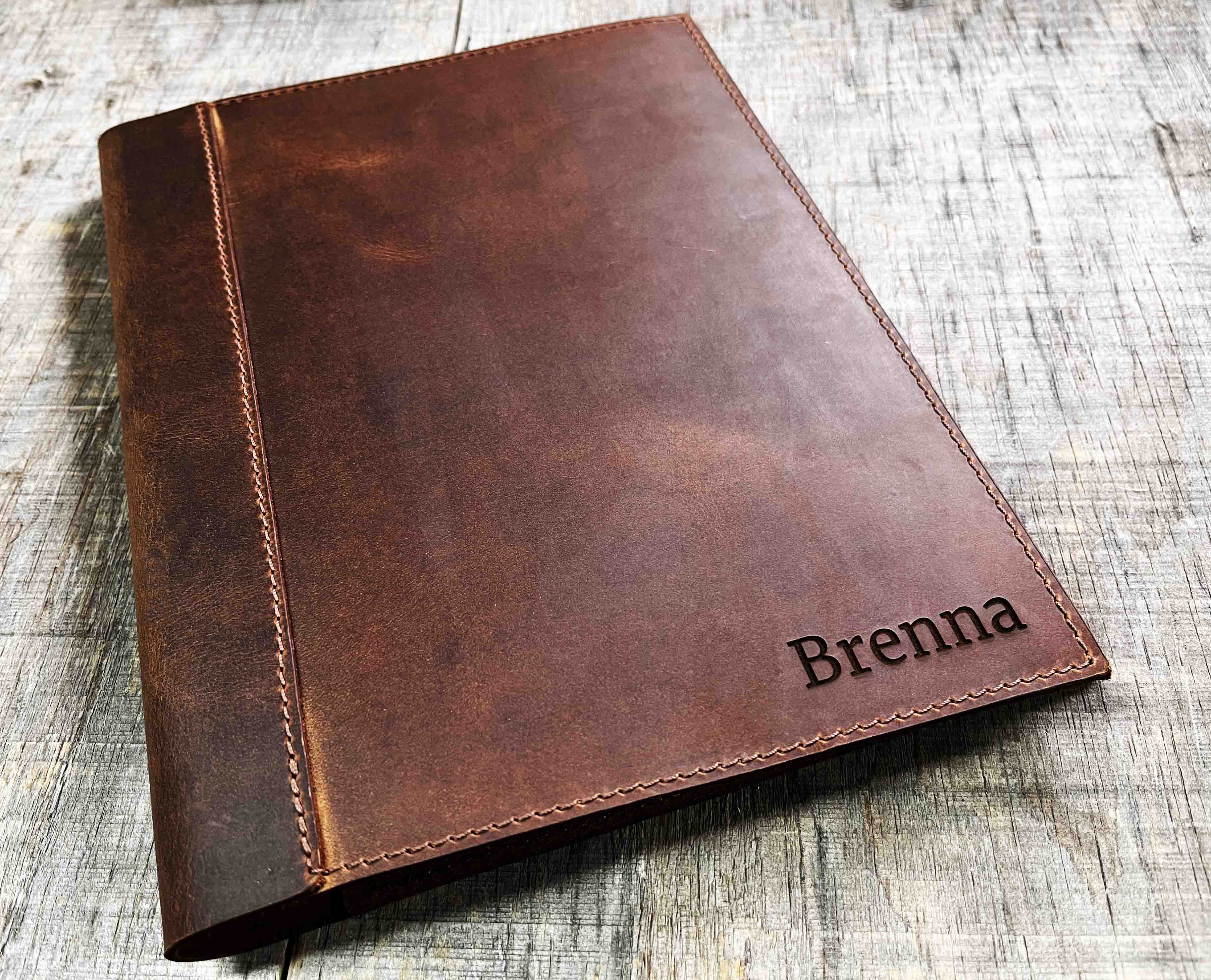 A brown, custom-engraved leather notebook cover featuring a geometric unicorn head design. The notebook is resting on an antique-style, ornate wooden desk alongside a glass inkwell and a feathered quill pen, creating a sophisticated and vintage aesthetic.