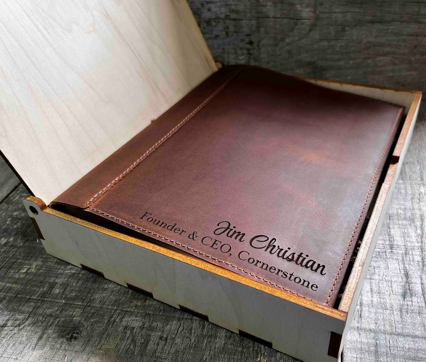 A brown, custom-engraved leather notebook cover featuring a geometric unicorn head design. The notebook is resting on an antique-style, ornate wooden desk alongside a glass inkwell and a feathered quill pen, creating a sophisticated and vintage aesthetic.