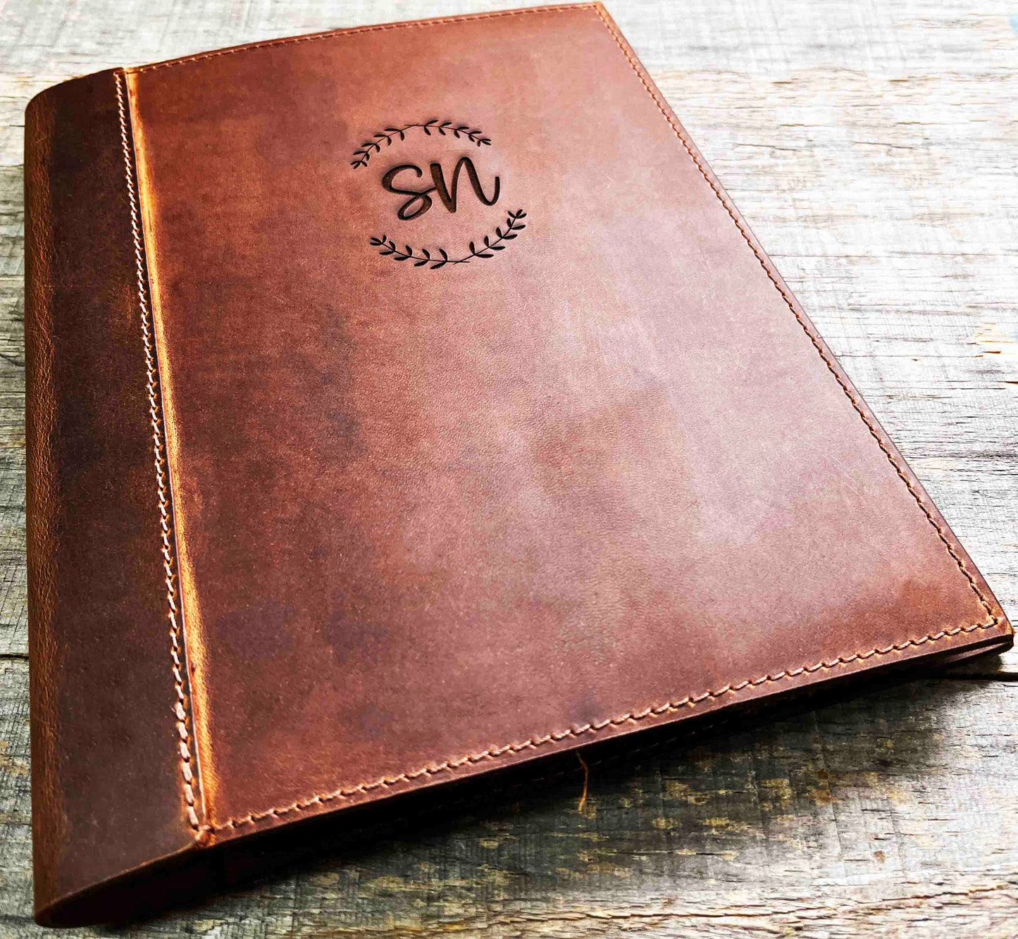 A brown, custom-engraved leather notebook cover featuring a geometric unicorn head design. The notebook is resting on an antique-style, ornate wooden desk alongside a glass inkwell and a feathered quill pen, creating a sophisticated and vintage aesthetic.